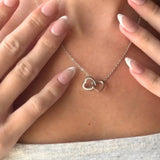 Woman wearing the silver double-heart necklace, holding both sides of the chain near her collarbone.