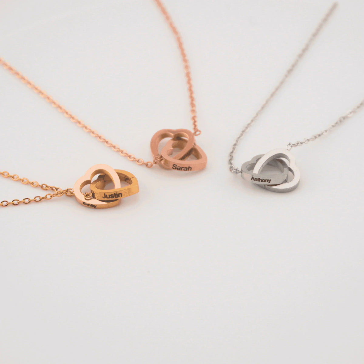 Three double-heart necklaces in gold, rose gold, and silver, each engraved with two sample names.